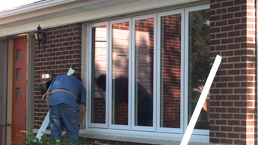 An Excel installer trimming a newly set window on a brick home.