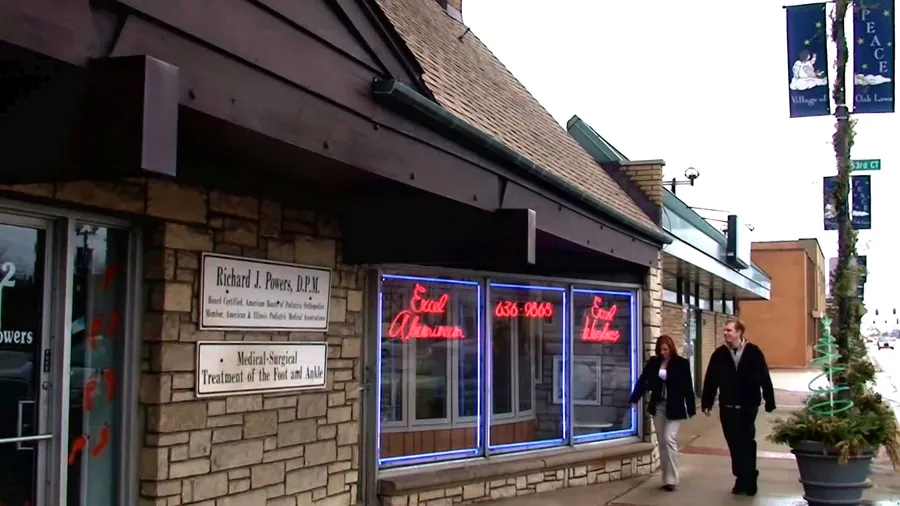 The Oak Lawn storefront at night, the original red Excel Aluminum neon glowing in the window.