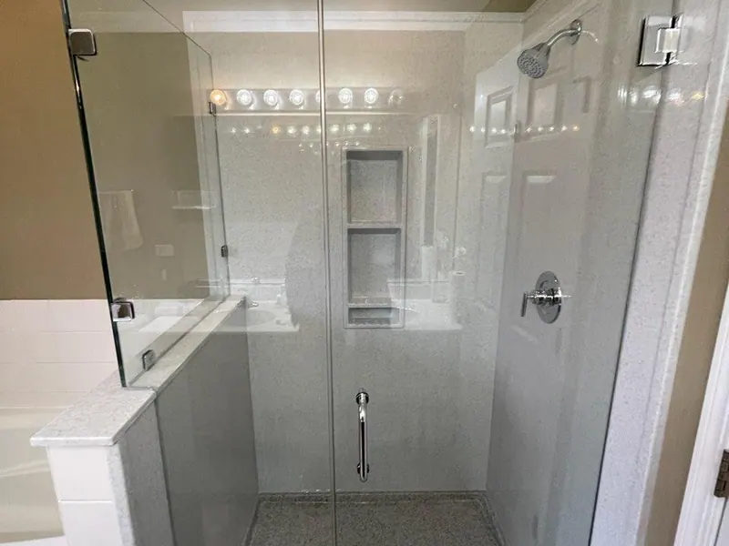 Frameless-glass walk-in shower with speckled solid-surface walls, a recessed niche, chrome fixtures, and a granite-look base, an Excel install