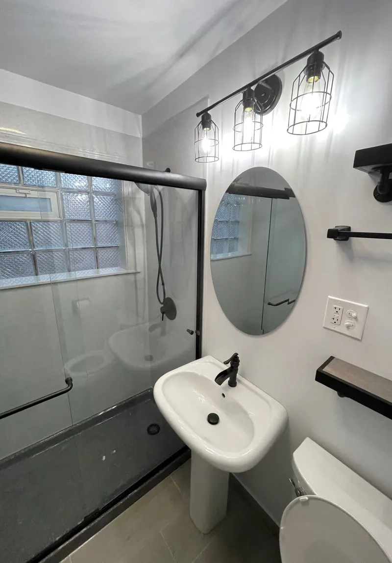 Finished Excel full bathroom remodel with a pedestal sink, an oval mirror, industrial vanity lighting, and a glass tub-shower